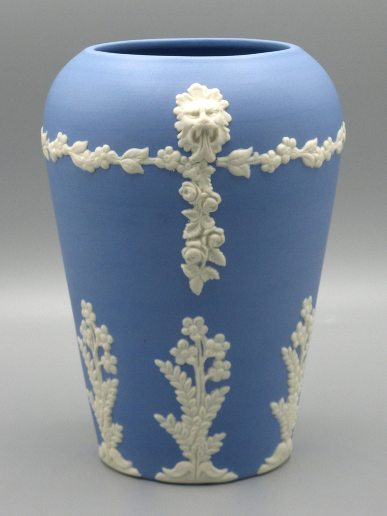 Blue vase with white flower and vine motifs and a lions head atop each side of the vase.